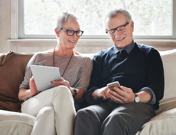 Mature Couple With Grey Hair Looking At Digital Tablet And Phone At Home My costs